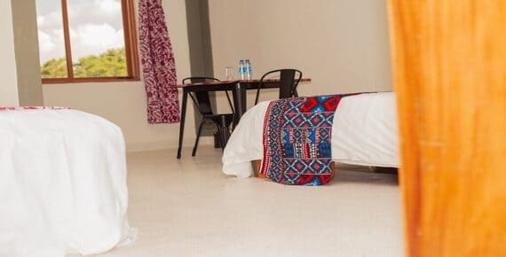 Sunlit guest room at Heritage Hotels Arua featuring vibrant African-patterned bedding and a cozy table by the window.
