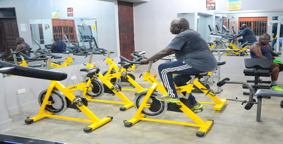 Hotel guests exercising on stationary bikes in the Heritage Hotels Arua fitness center, surrounded by modern workout equipment.